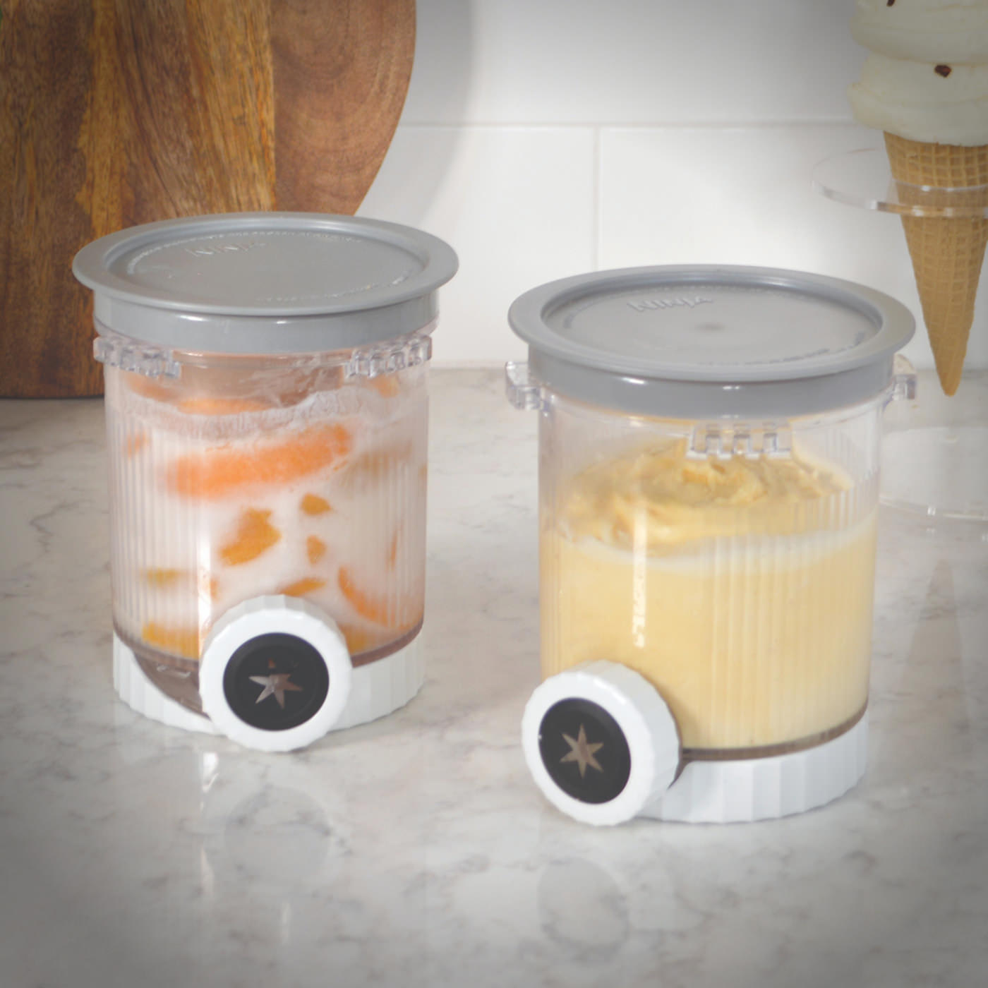 Two Ninja CREAMi dessert containers filled with swirled frozen treats with visible nozzles attached.